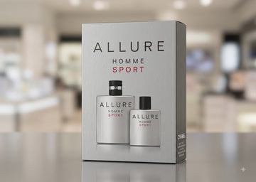 Allure Homme Sport cologne set in a silver-gray box, featuring two matching spray bottles with black caps, displayed on a reflective surface with a blurred store background.