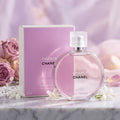Chanel Chance Eau Tendre perfume bottle and its matching pink box, styled on a marble surface with pink roses and white flowers against a soft lavender background.